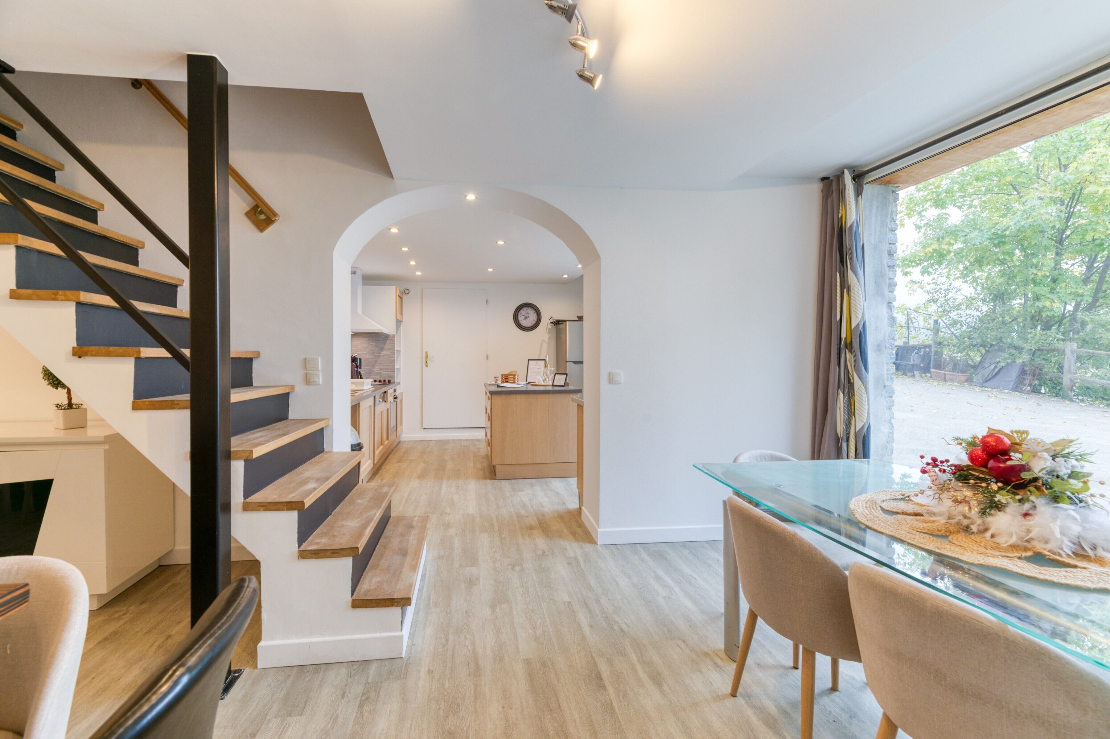 Een modern interieur met een trap, een glazen eettafel en uitzicht door een raam.