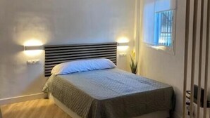 A bedroom with a bed, wooden flooring, a headboard, bedside lamps, and a window with curtains. - Mini Paradise Torremolino (Torremolinos)