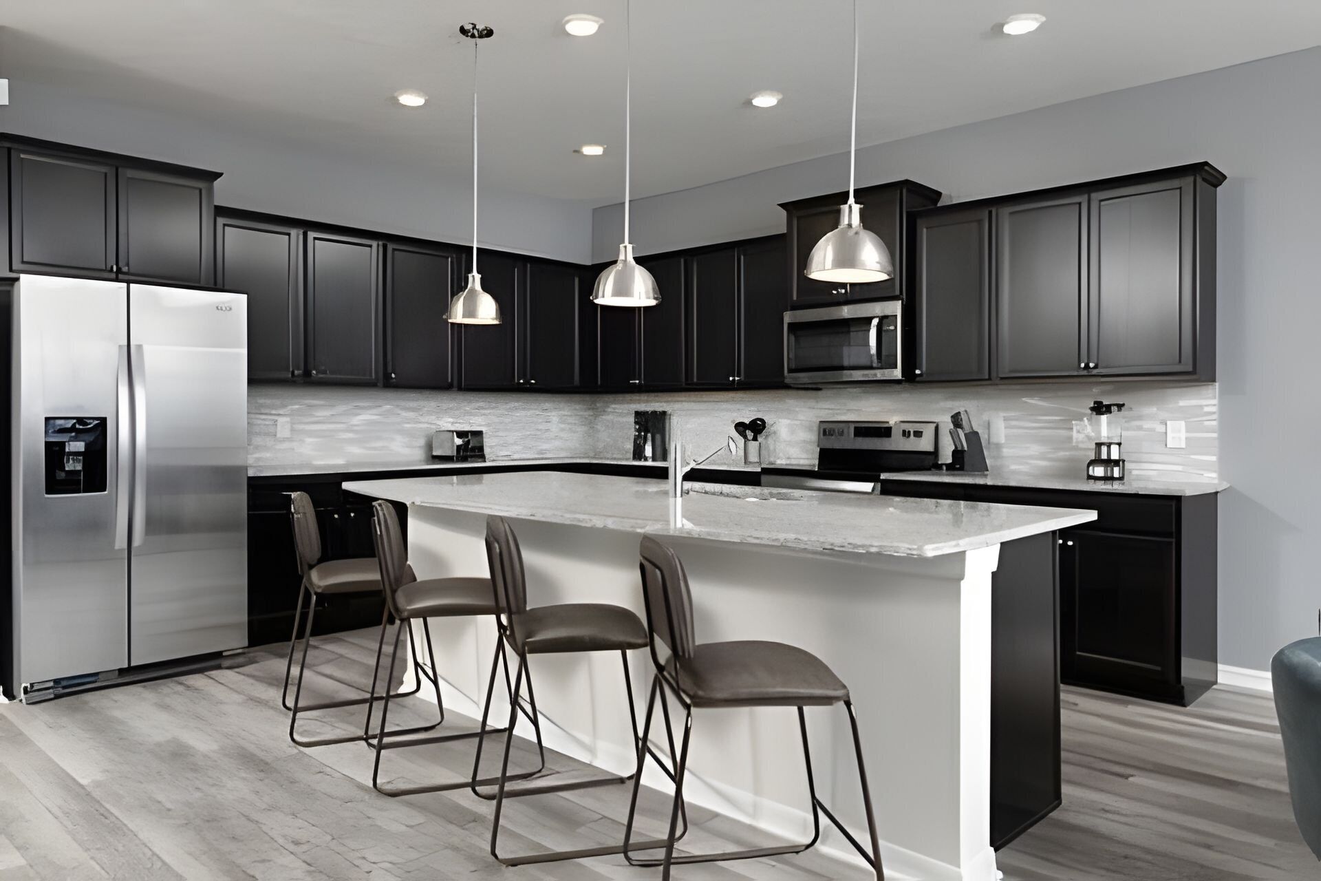 A modern kitchen with dark cabinets, stainless steel appliances, a central island with bar stools, pendant lighting, and a microwave above the island.