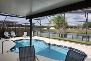 A covered outdoor swimming pool with lounge chairs, a view of a lake, and a grassy area.