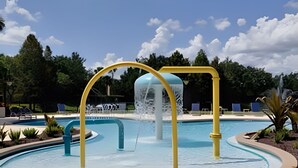 Una piscina con fuente central, rodeada de jardines, árboles y sillas de descanso.