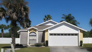 A single-story house with a garage, surrounded by palm trees and a white fence. - 10 Minutes to Disney! Pool Home Large Lot (Kissimmee)