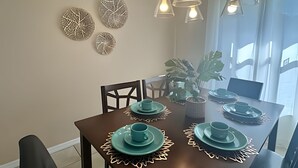 A dining area with a dark wooden table set for four, surrounded by chairs. There are decorative wall art pieces above the table and a potted plant to the side. - 10 Minutes to Disney! Pool Home Large Lot (Kissimmee)