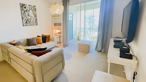 Ein modernes Wohnzimmer mit einer Couch, einem Fernseher und einem Balkon mit Vorhängen.