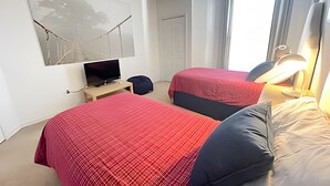 Ein Hotelzimmer mit zwei Betten, einem Fernseher, einem Schreibtisch und einem Fenster mit Vorhängen.