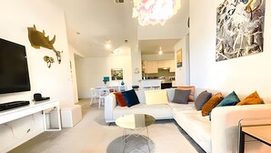 Ein modernes Wohnzimmer mit Flachbildfernseher, weißem Sofa und Essbereich im Hintergrund.