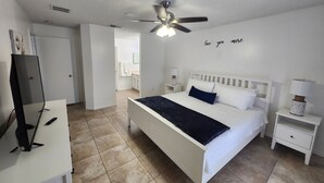 Een slaapkamer met een bed, nachtkastjes, een plafondventilator en een televisie.