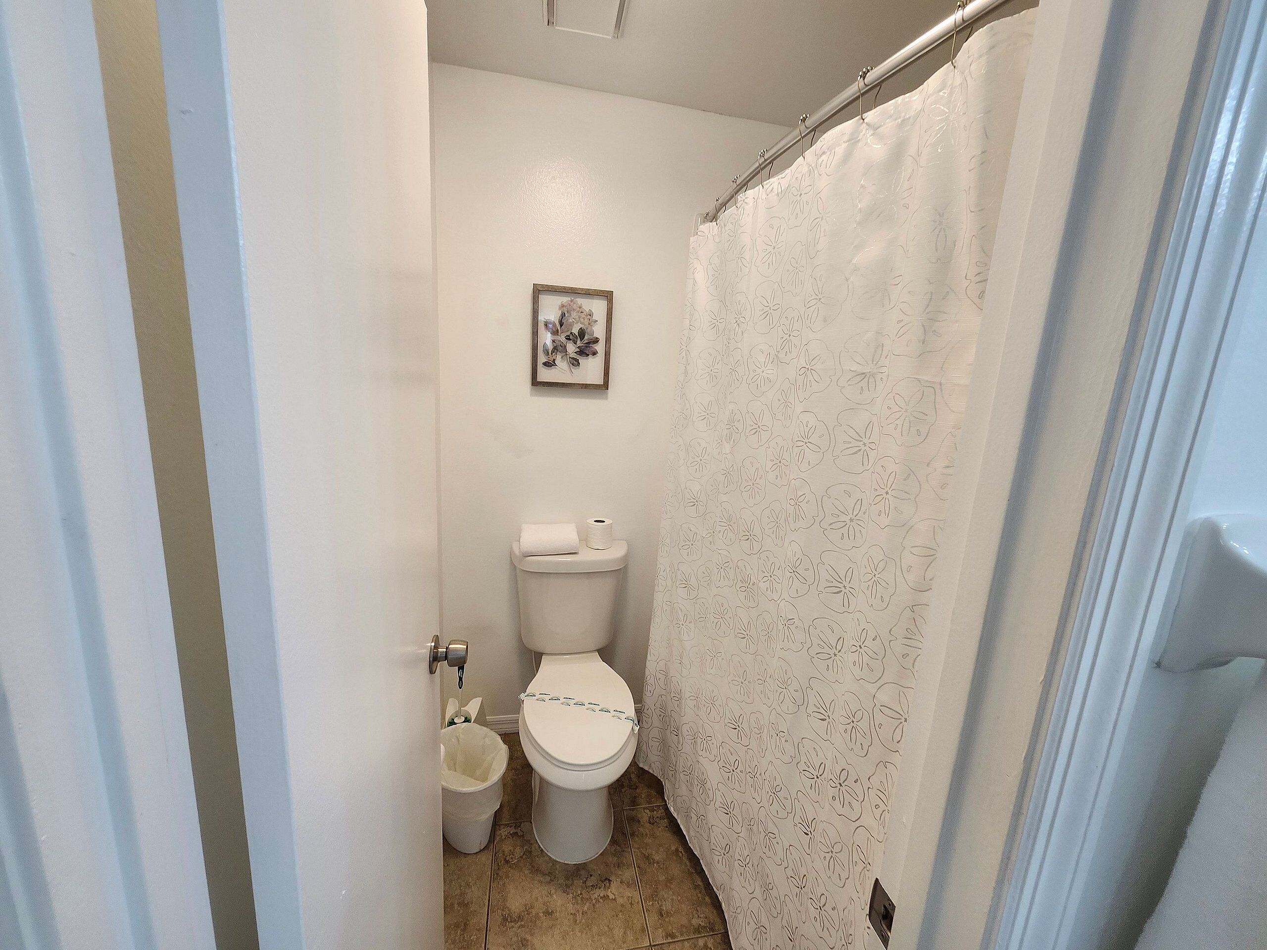 A small bathroom with a toilet, a trash can, and a shower curtain.