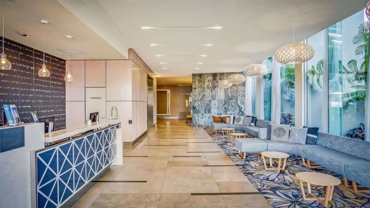 A modern hotel lobby with a reception desk, seating area, and large windows with plant views.