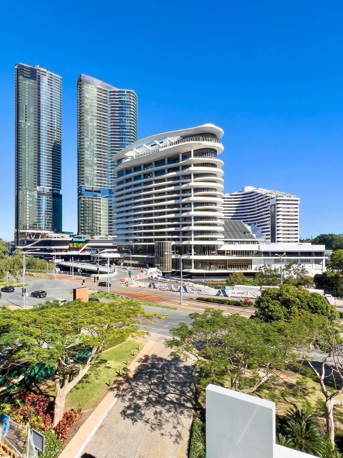 Un horizonte urbano moderno con rascacielos, una estructura curva con balcones y un parque bien cuidado con árboles y senderos.