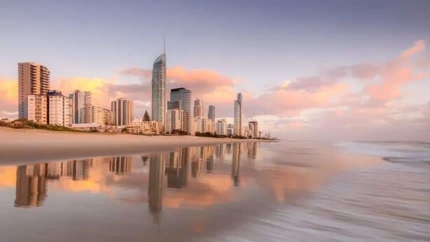 Paisagem costeira urbana com arranha-céus e uma praia calma que reflete o horizonte.