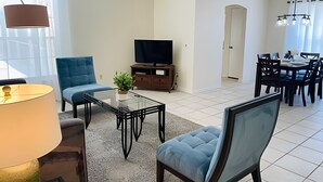 A living room with a sofa, a coffee table, a TV, and a dining area with chairs and a table. - Huge Lot, Private Pool Home Centrally Located (Kissimmee)