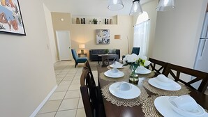 A dining area with a table set for four, a sofa, and a lamp in the background. - Huge Lot, Private Pool Home Centrally Located (Kissimmee)