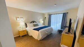 A hotel room with a bed, bedside tables, a desk, a chair, a TV, and a window with curtains. - Huge Lot, Private Pool Home Centrally Located (Kissimmee)