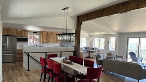 A spacious kitchen with wooden cabinets, a stainless steel refrigerator, and a large island with a dining table and red chairs. - Beautiful, newly renovated mountain home. (Golden)