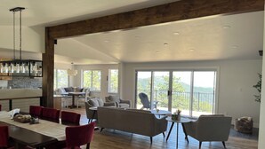 A spacious living area with a wooden floor, a dining table with red chairs, and a balcony with a view of the mountains. - Beautiful, newly renovated mountain home. (Golden)