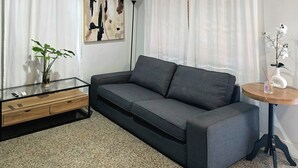 A modern living room with a grey sofa, a glass coffee table, a small wooden side table, and a floor lamp. - Charming 1-bedroom house in marvelous Fort Lauderdale with WiFi, AC, Parking (Fort Lauderdale)