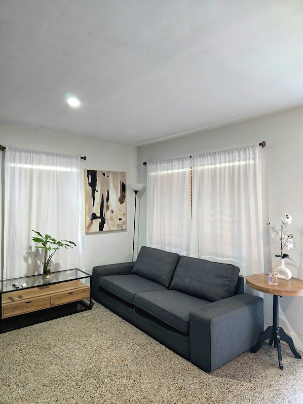A modern living room with a grey sofa, a glass coffee table, a small wooden side table, and a floor lamp.