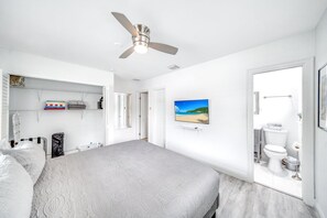 A bedroom with a bed, a ceiling fan, a TV on the wall, and a bathroom visible through an open door. - Heated Pool! Close To Beach+Restaurants & Shops! (Fort Lauderdale)