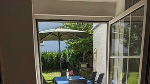 Un patio con mesa y sillas, una puerta que da a un jardín y un felpudo.