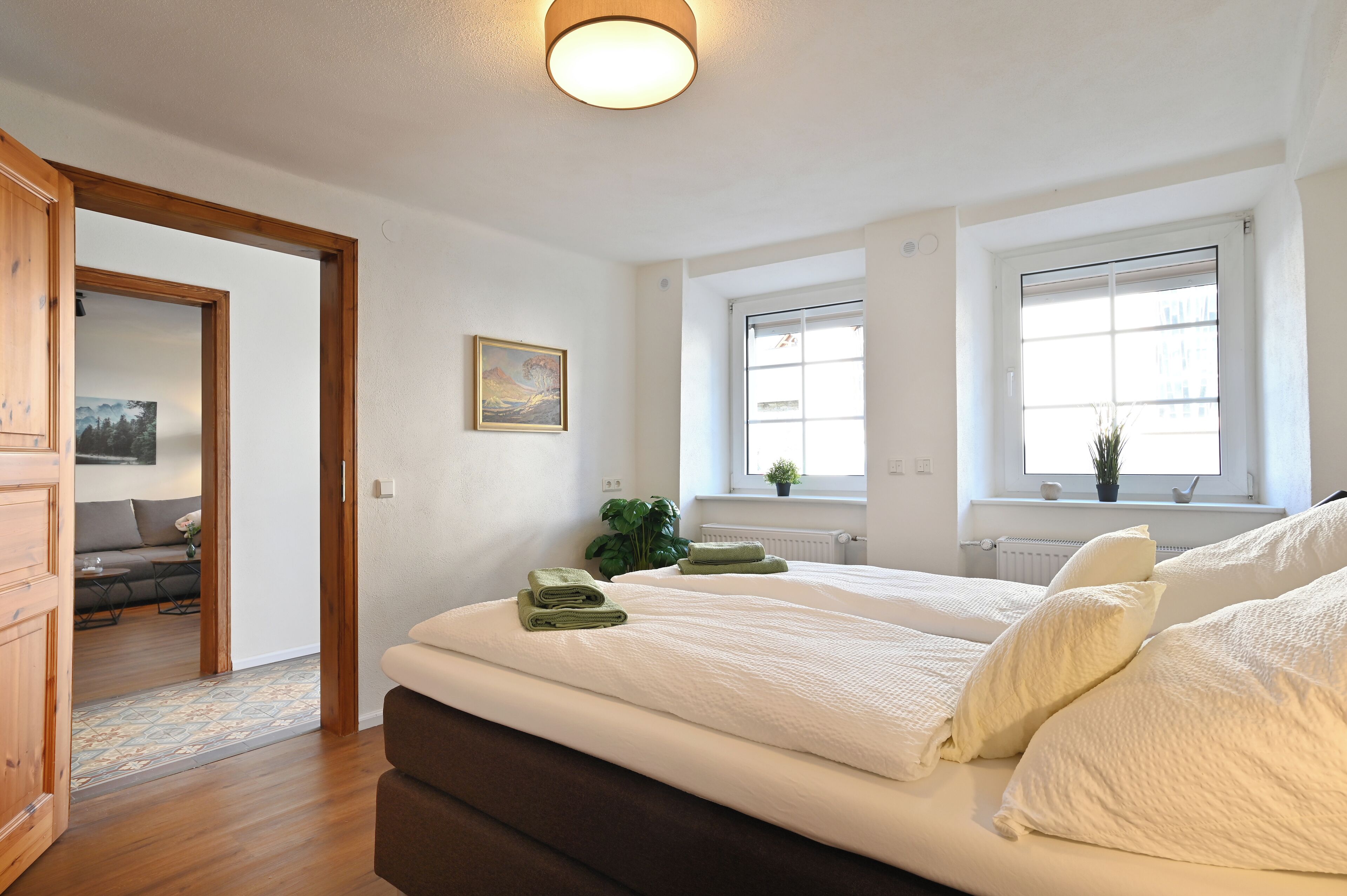 Hotellihuone, jossa on kaksi sänkyä, puinen vaatekaappi, taulu ja näkymä ulos suurista ikkunoista.