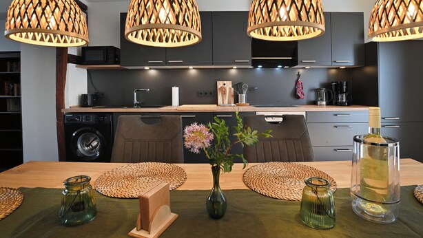 Una cocina moderna con armarios oscuros, encimera de madera y lámparas colgantes con diseño de celosía.