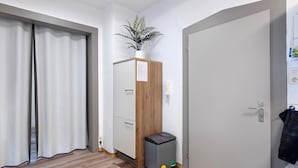 Habitación de hotel con un armario de madera, un cesto de basura, una planta en maceta y una puerta con una toalla colgada.