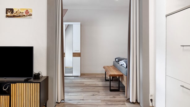 Un pasillo con un televisor sobre un mueble de madera, un banco, un sofá y una puerta que da a otra habitación.