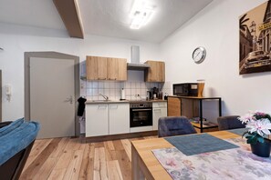 Una cocina compacta con armarios blancos, un microondas y un comedor con mesa y sillas.