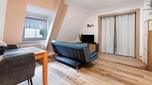 Una sala de estar moderna con sofá, mesa de comedor, televisor y ventana con cortinas.