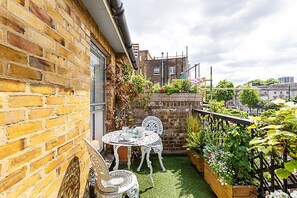 A small patio with a round table and chairs, surrounded by potted plants and a brick wall. - Modern Borough Retreat With Private Terrace (London)