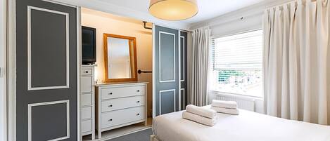 Quarto de hotel com cama, penteadeira, espelho e janela com cortinas.