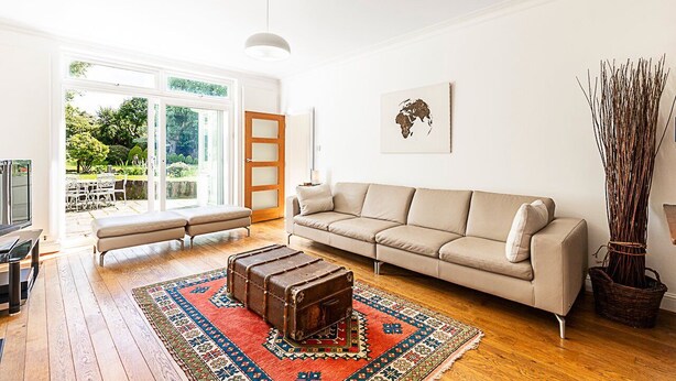 Ein geräumiges Wohnzimmer mit einem beigen Sofa, einem Holztisch und einem gemusterten Teppich.