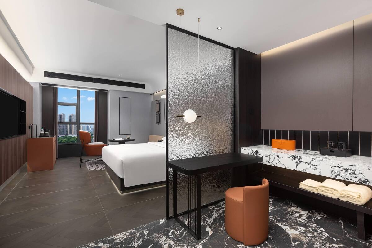 Quarto de hotel moderno com uma cama grande, uma escrivaninha, um espaço de estar e um banheiro com bancada de mármore.