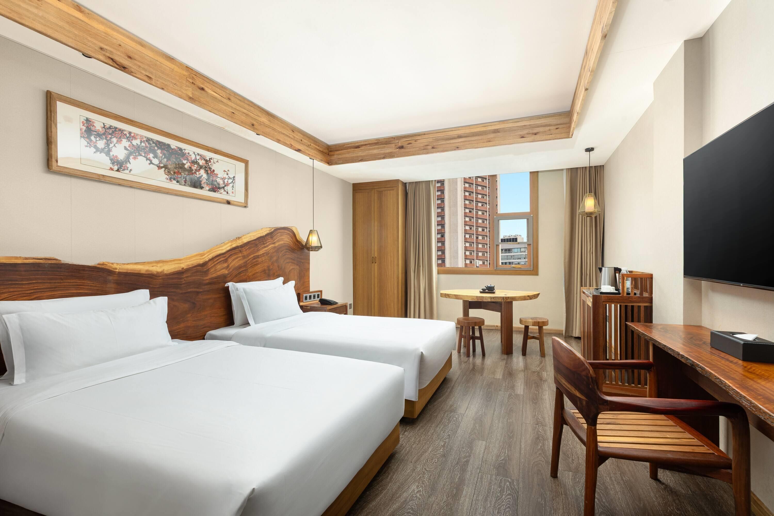 A hotel room with two beds, a desk, a chair, a TV, and a window with a city view.