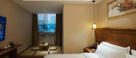 A hotel room with a bed, bedside table, lamp, and a painting on the wall.