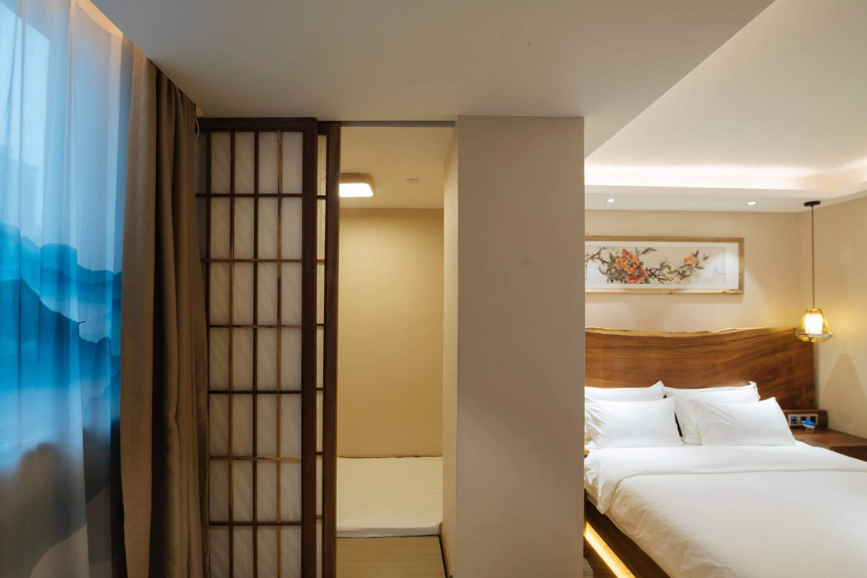 A hotel room with a bed, a nightstand, a wall-mounted lamp, and a painting.