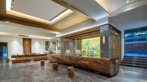 A reception area with a wooden reception desk, marble flooring, and a large painting on the wall.