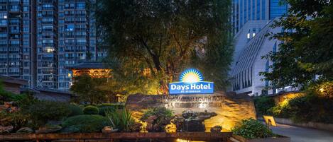 A hotel entrance with a sign, a landscaped garden, and a cityscape in the background.