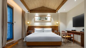 A hotel room with a large bed, wooden headboard, bedside tables, a desk, and a TV.