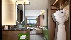 Casa de banho de hotel moderna com um espelho grande, toucador com lavatório, prateleira verde para toalhas e um roupão num suporte.