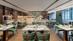 Um restaurante moderno com cadeiras estofadas em verde, mesas de mármore e um balcão central.