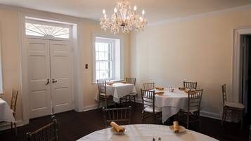 A dining area with white tables and chairs, a chandelier, and a large window.
