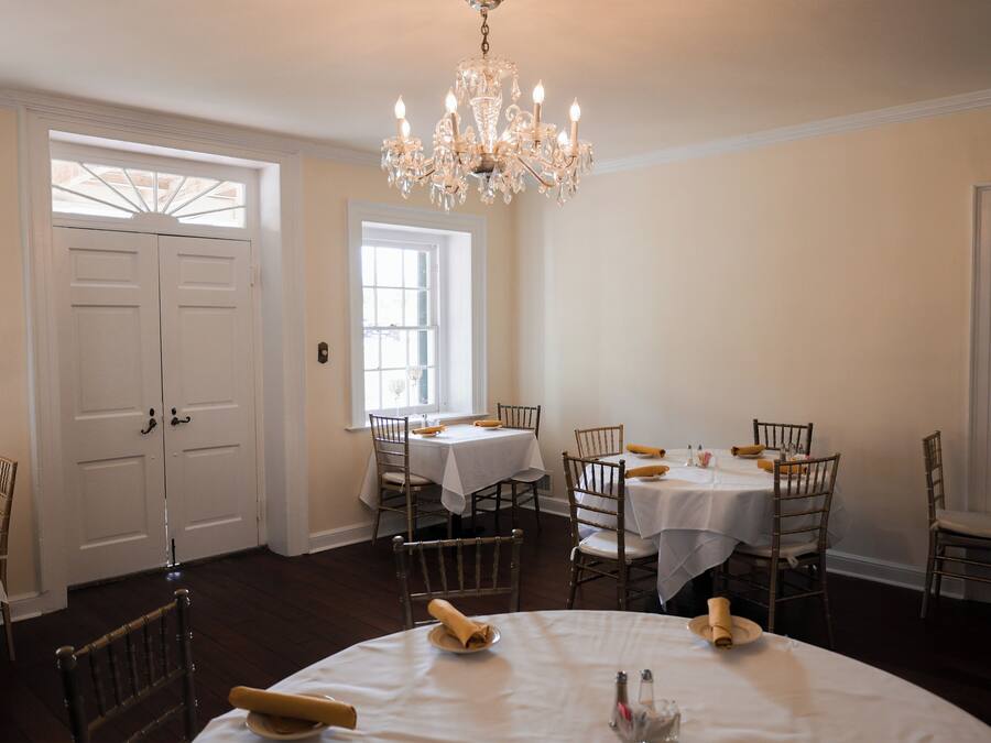 A dining area with white tables and chairs, a chandelier, and a large window.