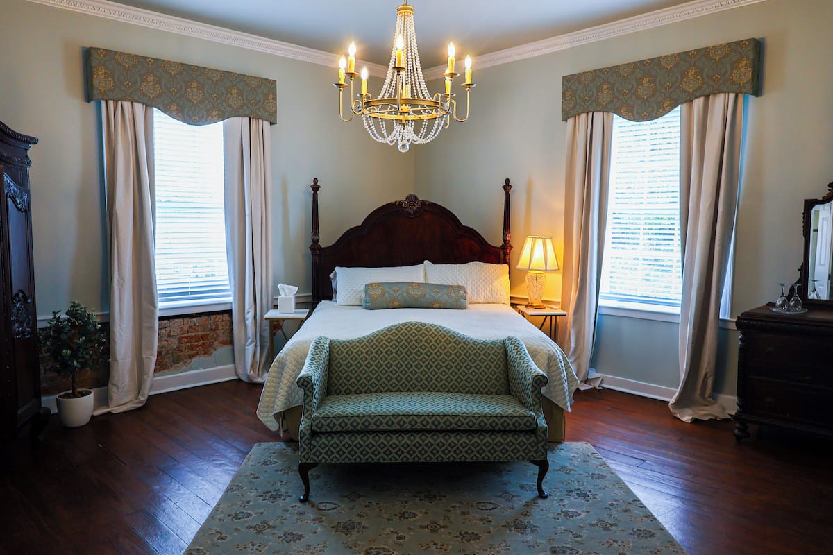 A bedroom with a large bed, a chandelier, and a green armchair.