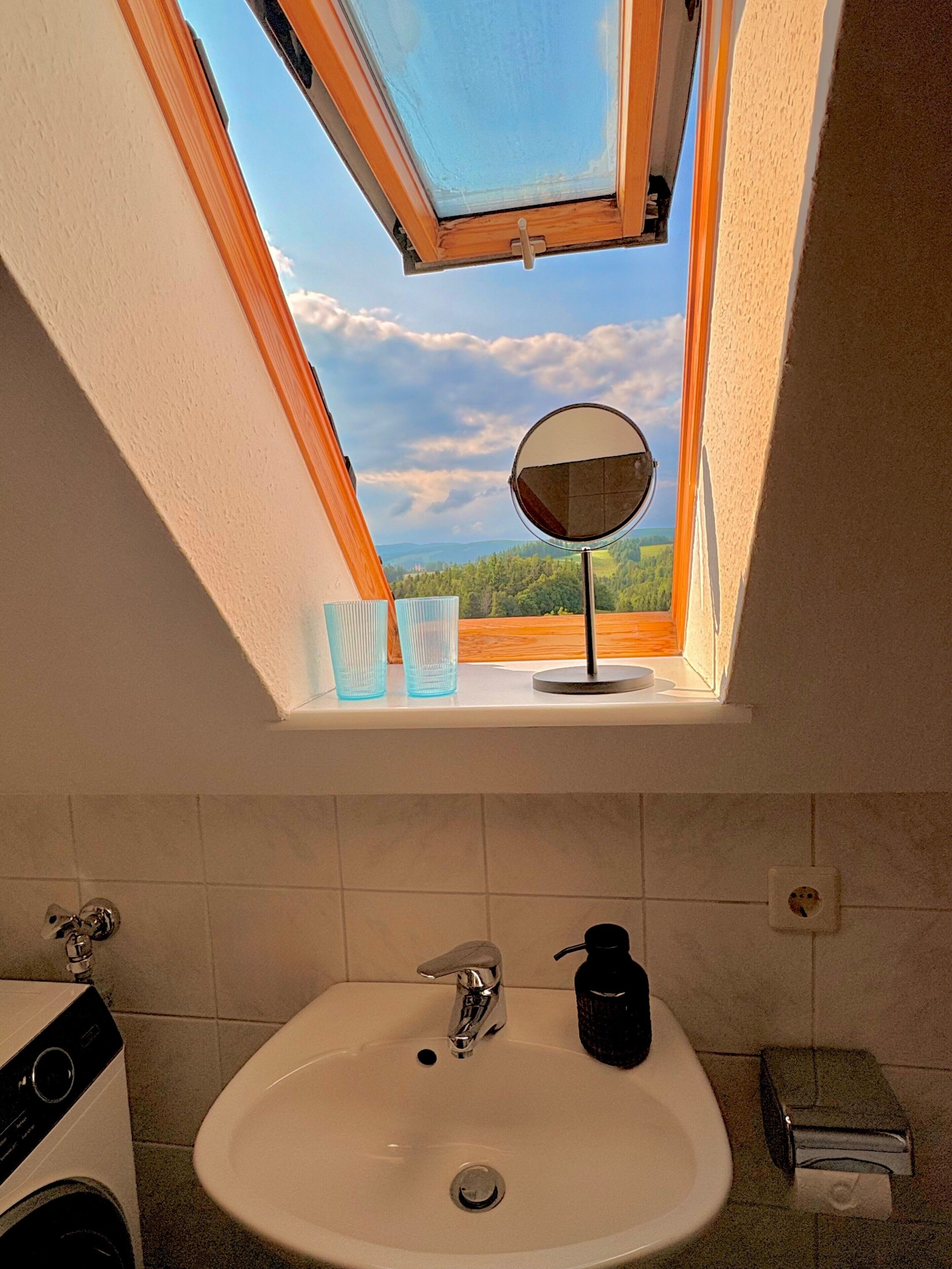 Ein Oberlicht über einem Badezimmerwaschbecken mit Spiegel, zwei Gläsern und einer Seifenspender.