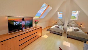 A bedroom with a TV, two beds, skylights, and a wooden dresser. - Apartment with Panoramic View (Sankt Märgen)