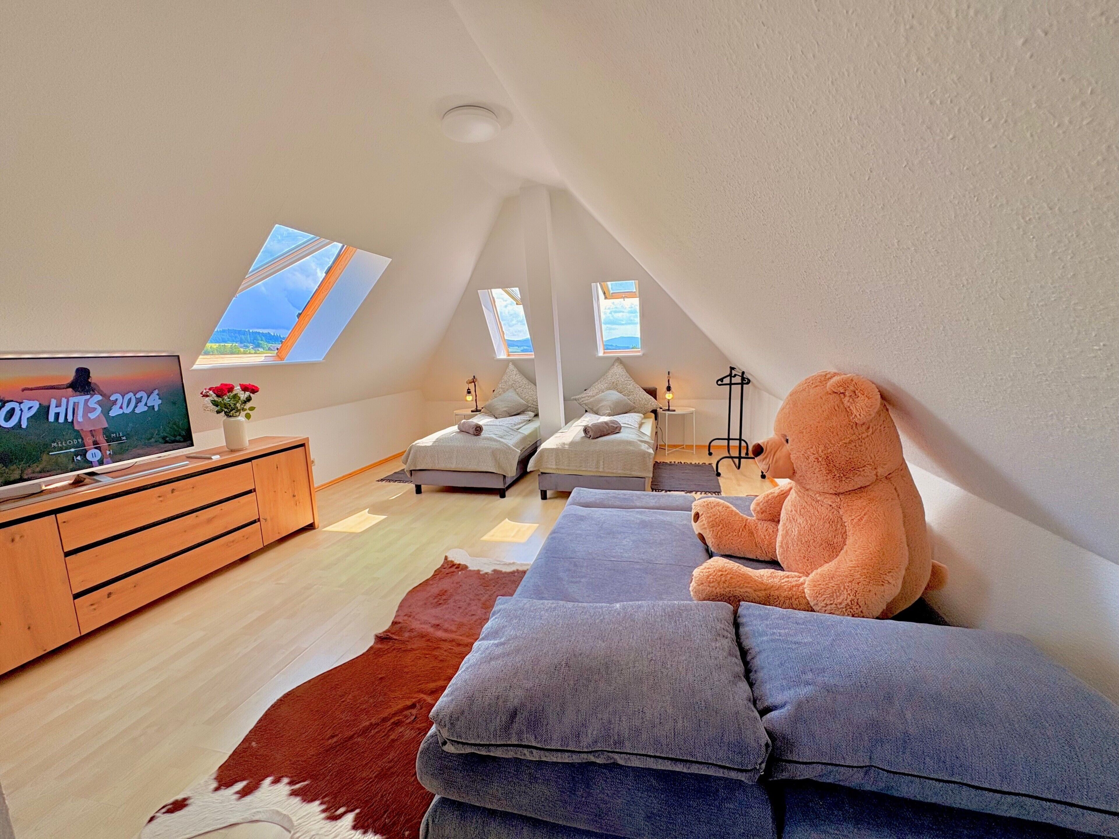 A cozy loft bedroom with a large TV, a teddy bear, and a cowhide rug.