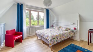 A bedroom with a bed, a red chair, a window with curtains, and a radiator. - Le Logis - Charmante Maison Proche Plage (Téteghem-Coudekerque-Village)