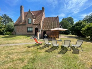 A two-story brick house with a tiled roof, a patio with outdoor furniture, and a well-maintained lawn.
